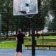 Junger Mann spielt Basketball an einer Outdoor Basketballanlage von Kenguru Pro auf einem öffentlichen Sportplatz mit Gitterzaun