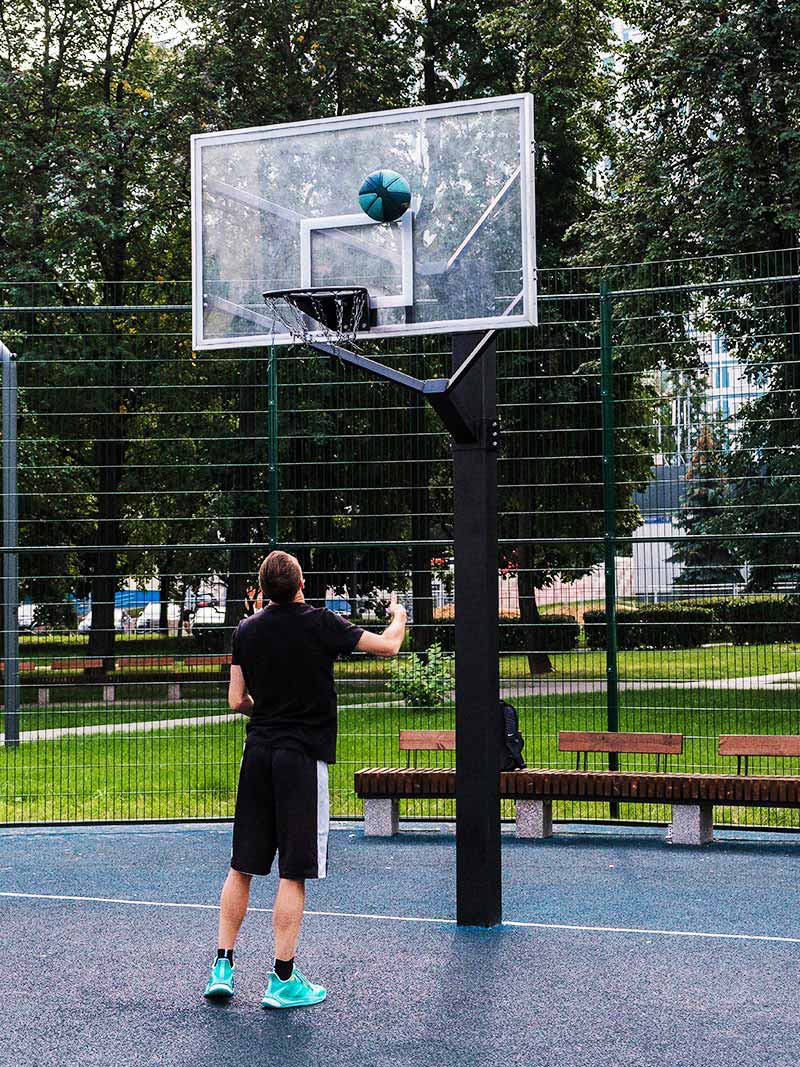Junger Mann spielt Basketball an einer Outdoor Basketballanlage von Kenguru Pro auf einem öffentlichen Sportplatz mit Gitterzaun