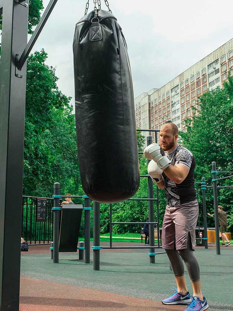 Mann beim Boxtraining mit einem Kenguru Pro Boxsack in einem modernen Outdoor-Fitnesspark.