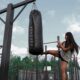Junge Frau trainiert Kicktechniken am Outdoor Boxsack von Kenguru Pro im Calisthenics Park