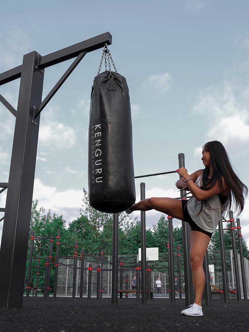 Junge Frau trainiert Kicktechniken am Outdoor Boxsack von Kenguru Pro im Calisthenics Park