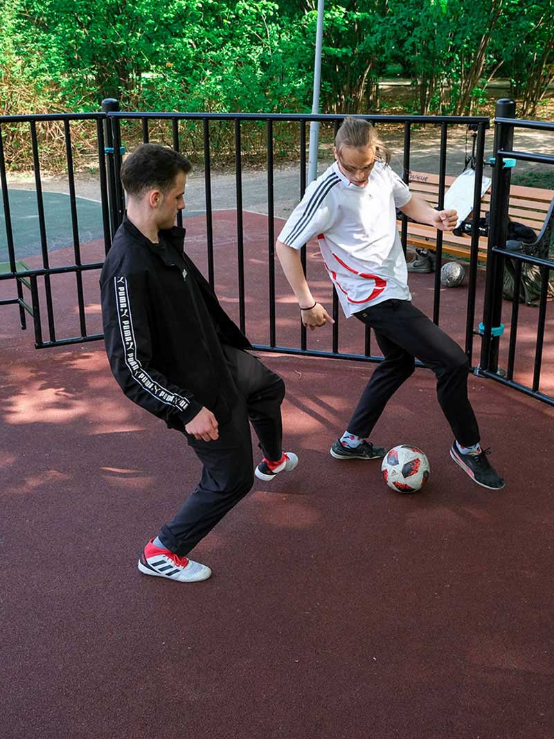 Zwei junge Männer spielen Panna Fußball auf einem Outdoor-Kleinspielfeld mit rotem Bodenbelag