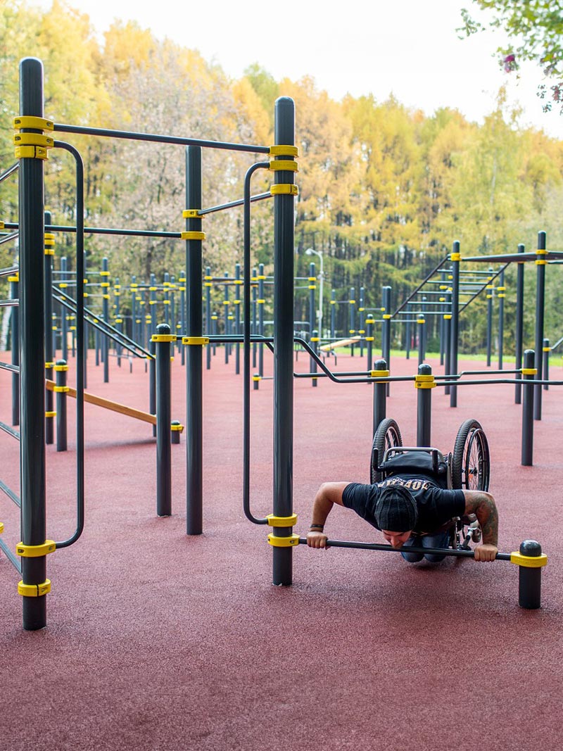 Rollstuhlfahrer führt Liegestütze an einer niedrigen Stange einer Calisthenics Anlage aus