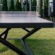 Moderne Tischtennisplatte Outdoor mit robustem Design und perforiertem Netz, aufgestellt auf einer grünen Rasenfläche.