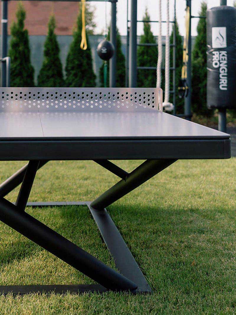 Moderne Tischtennisplatte Outdoor mit robustem Design und perforiertem Netz, aufgestellt auf einer grünen Rasenfläche.
