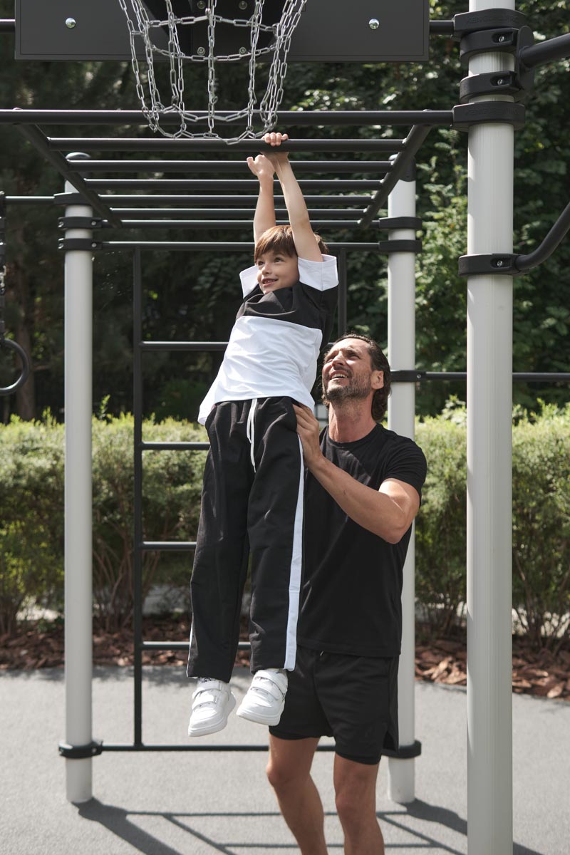 Vater hilft seinem Sohn beim Hangeln an einer Hangelleiter einer Calisthenics Anlage von Kenguru Pro im Freien