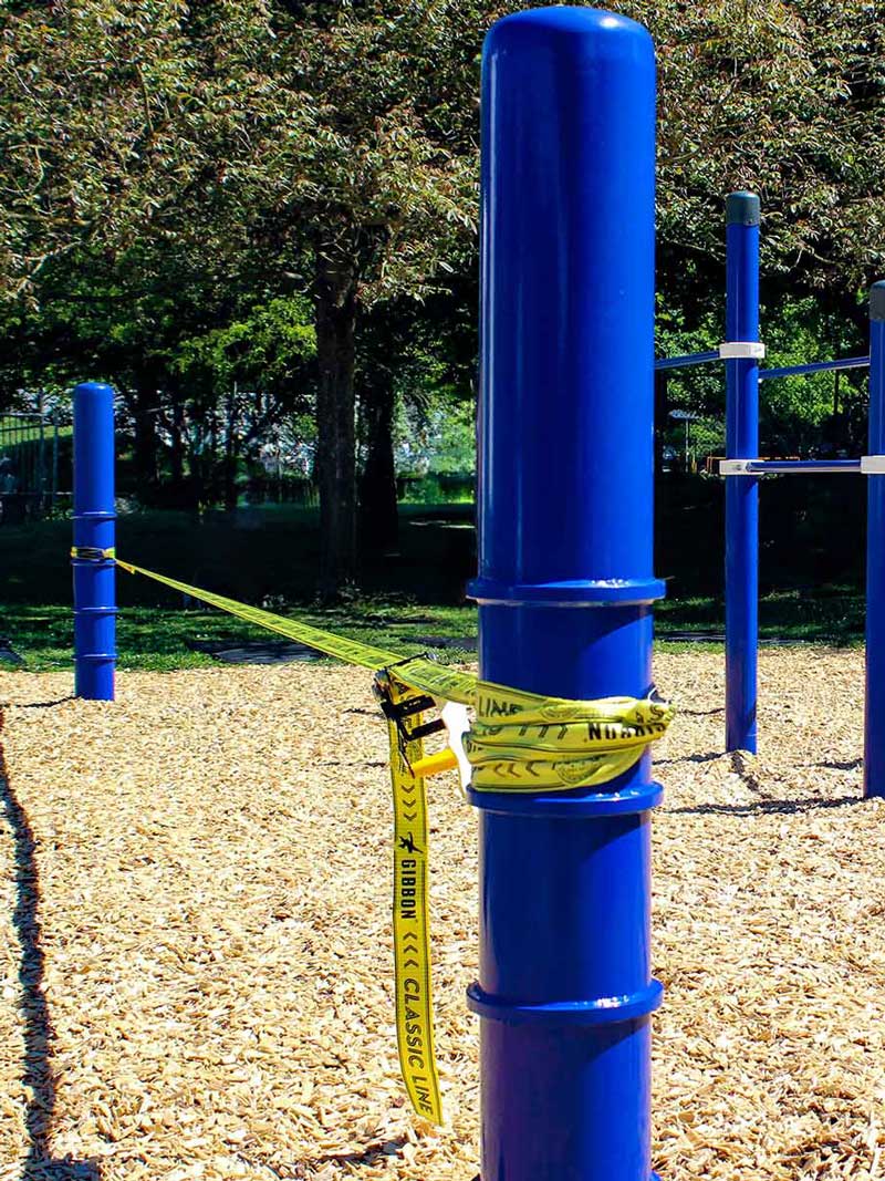 Zwei blaue Slackline Pfosten von Kenguru Pro spannen ein gelbes Trainingsband zum Balancieren im öffentlichen Park