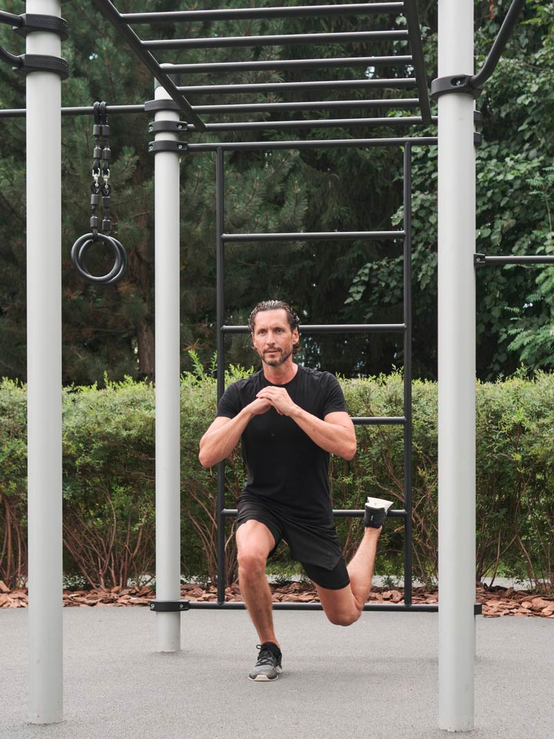 Mann macht Ausfallschritt an einer Outdoor Calisthenics Anlage mit Sprossenwand.