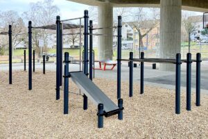Calisthenics Park in Kornwestheim „Am Brückle“ unter der Gumpenbackbrücke nahe Stuttgart – ausgestattet mit Klimmzugstangen, Dip-Barren, Schrägbank und Monkey Bars. Die Anlage steht auf stoßdämpfendem Rindenmulch und bietet optimale Bedingungen für funktionelles Training im öffentlichen Raum. Ideal für alle Altersgruppen, um Kraft, Koordination und Ausdauer im Freien zu verbessern.