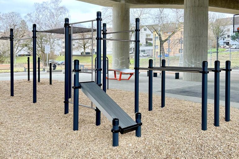 Calisthenics Park in Kornwestheim „Am Brückle“ unter der Gumpenbackbrücke nahe Stuttgart – ausgestattet mit Klimmzugstangen, Dip-Barren, Schrägbank und Monkey Bars. Die Anlage steht auf stoßdämpfendem Rindenmulch und bietet optimale Bedingungen für funktionelles Training im öffentlichen Raum. Ideal für alle Altersgruppen, um Kraft, Koordination und Ausdauer im Freien zu verbessern.