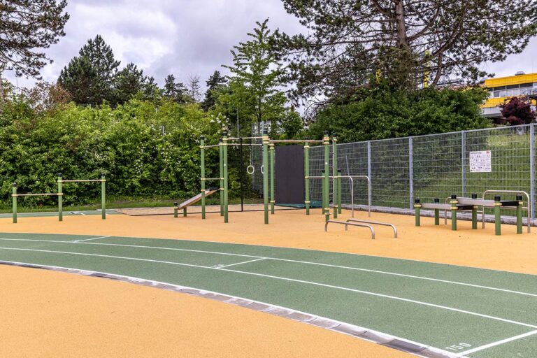 Calisthenics Park am Berufsschulzentrum Ravensburg – ausgestattet mit vielfältigen Trainingsgeräten wie Klimmzugstangen, Turnringen, Schrägbank, Sprossenwand, Hürden und Dip-Barren. Die Anlage steht auf einem gelenkschonenden Gummiboden direkt an einer Laufbahn und ist ideal für funktionelles Outdoor-Training im schulischen und öffentlichen Bereich. Umgeben von viel Grün bietet der Park optimale Bedingungen für Kraft- und Koordinationstraining im Freien.