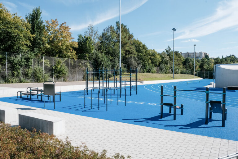 Der moderne Calisthenics Park in Villingen-Schwenningen mit blauen Gummiböden, Klimmzugstangen, Barren und einer angrenzenden Laufbahn vor einer dichten Waldkulisse unter blauem Himmel