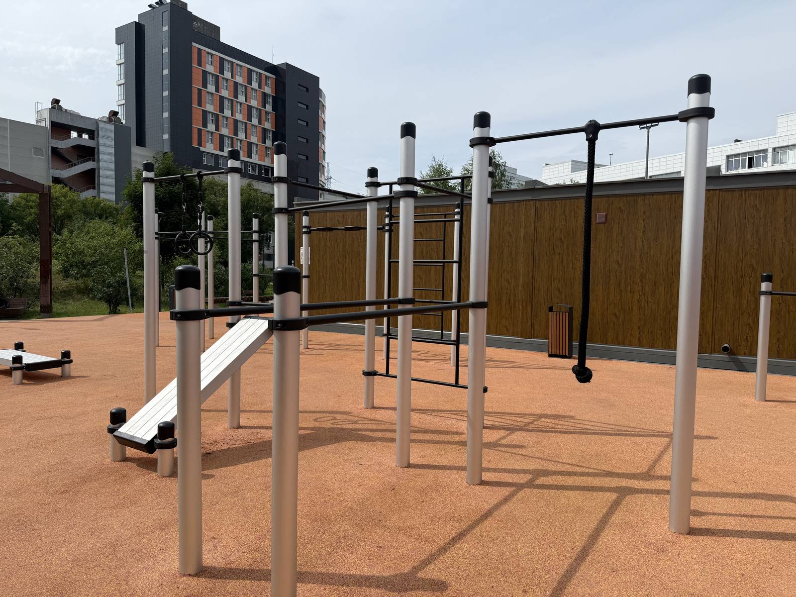Calisthenics Anlage von KENGURU PRO mit Schrägbank, Sprossenwand, Reckstangen in mehreren Höhen und Boxbirne auf ockerfarbenem Belag