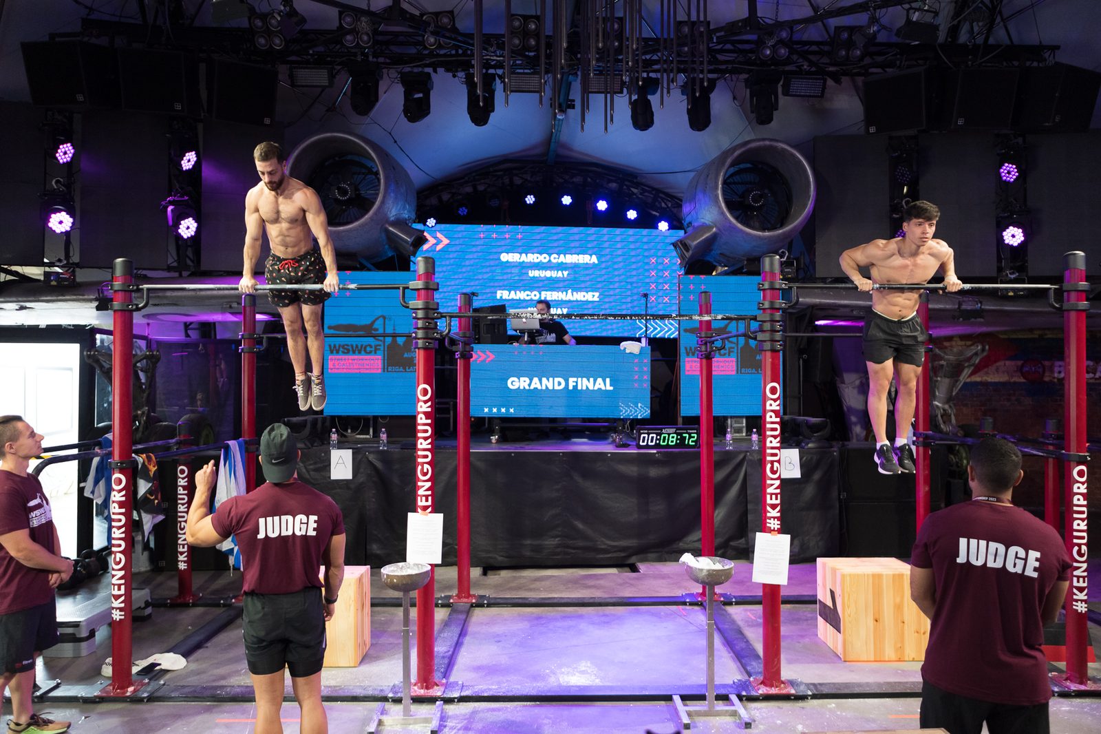 Zwei Athleten im Finale eines Street-Workout-Wettkampfs auf einer Bühne mit Calisthenics Anlage von KENGURU PRO, davor die Jury