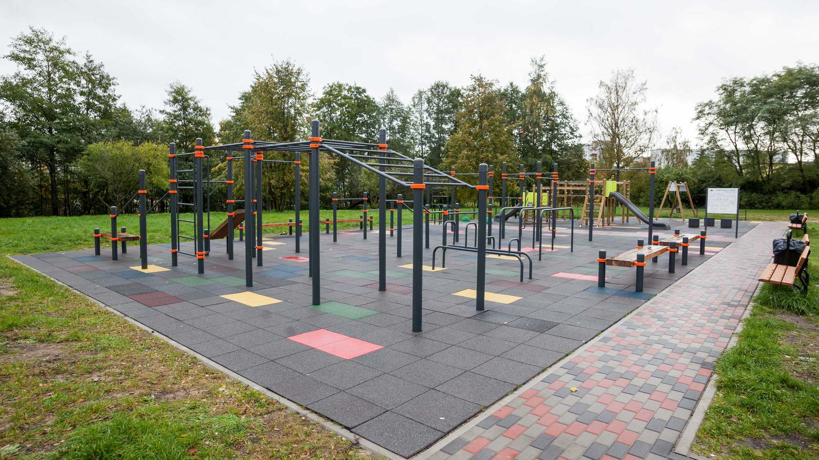 Generationenpark mit Calisthenics Anlage von KENGURU PRO in Riga: viele Stationen auf Fallschutzplatten, gepflasterter Zugangsweg und Sitzbank