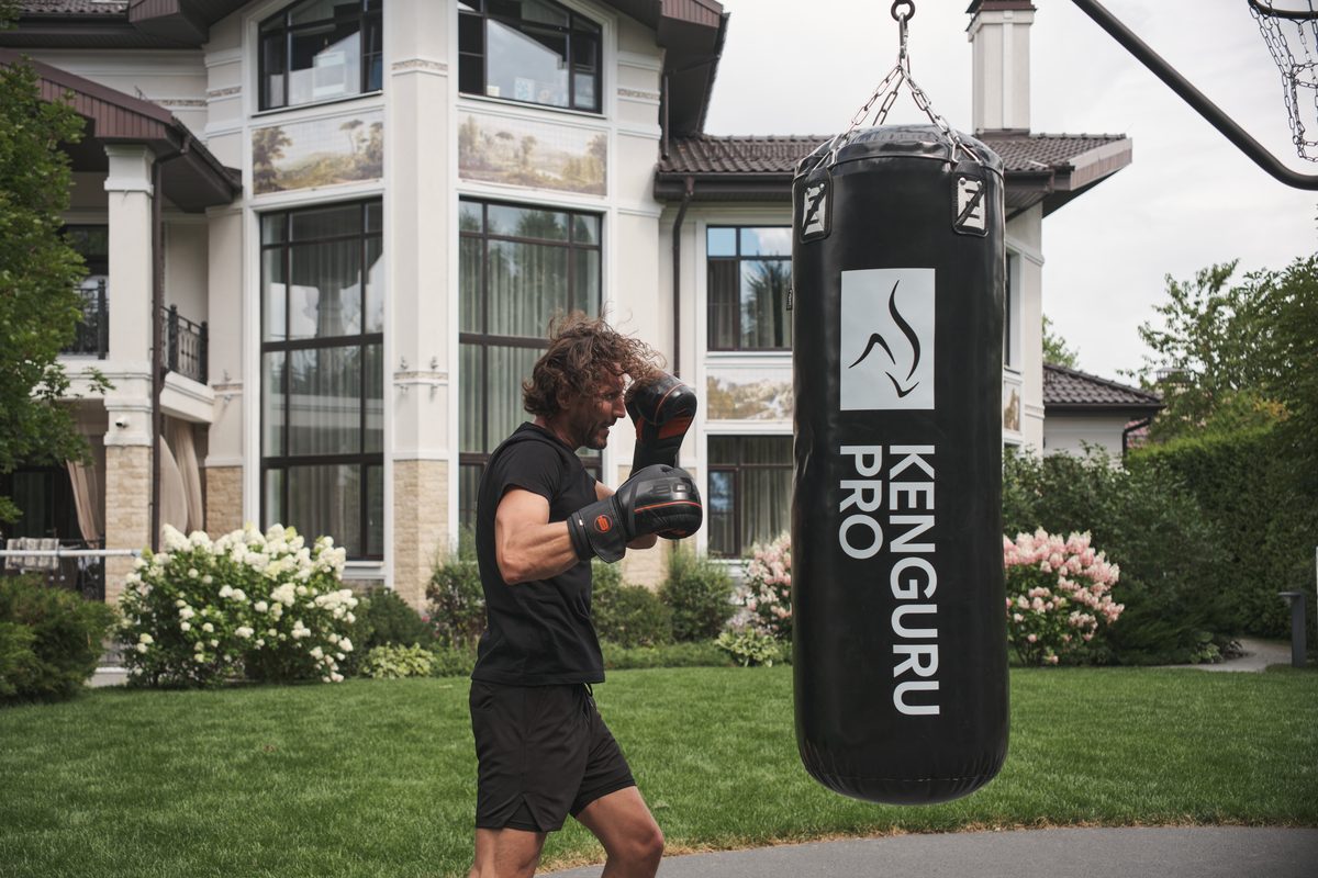 Mann mit Boxhandschuhen trainiert an einem Boxsack von KENGURU PRO im Garten vor einem Wohnhaus