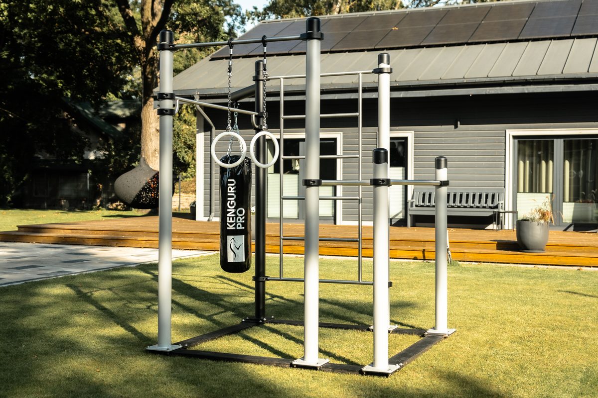 Mobile Calisthenics Station von KENGURU PRO mit Boxsack, Turnringen und Sprossenwand auf dem Rasen eines Gartens