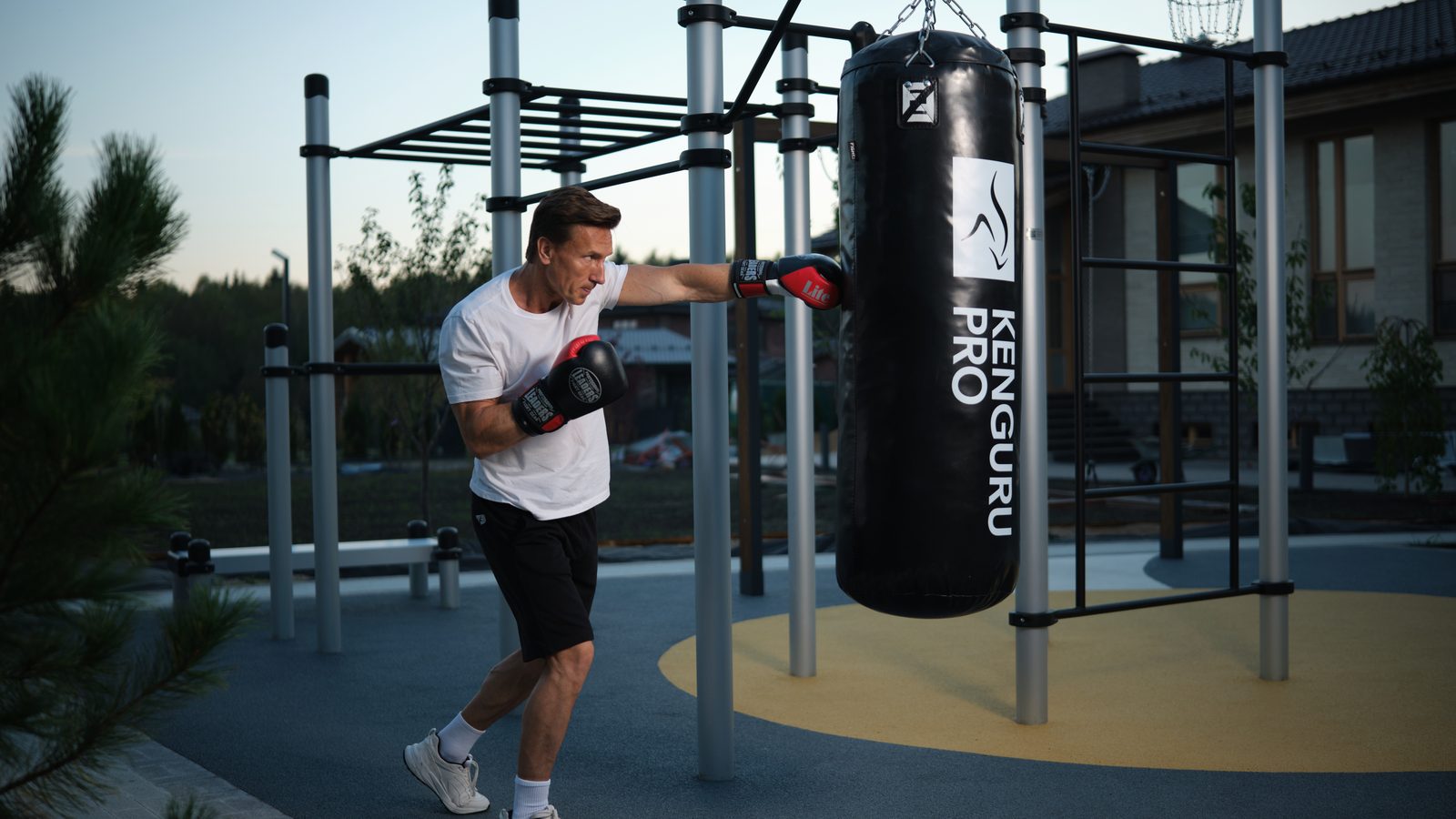 Mann trainiert Schlagkombinationen an einem Outdoor Boxsack von KENGURU PRO an einer Calisthenics Anlage auf Fallschutzbelag