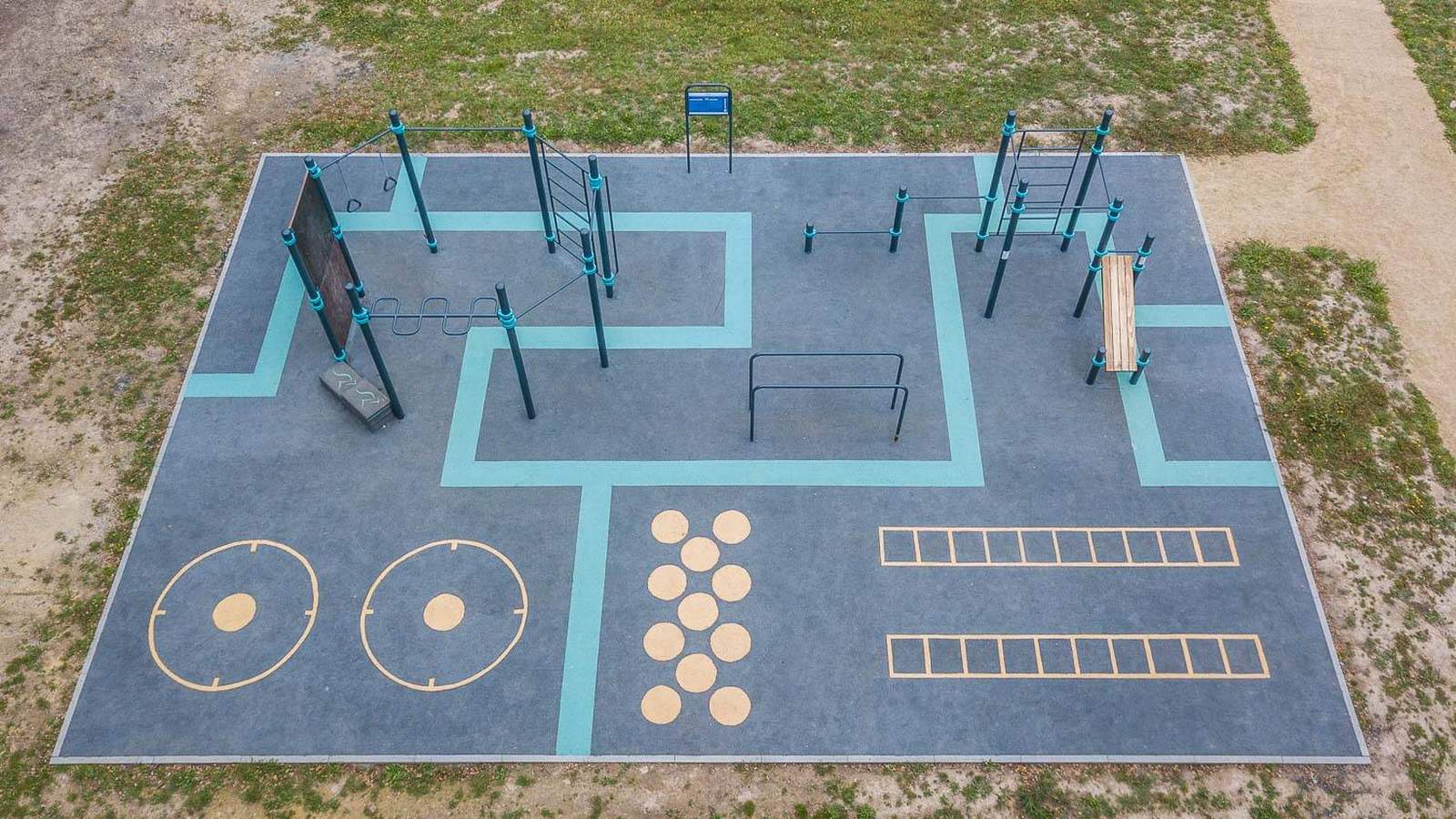 Outdoor Trainingsplatz von KENGURU PRO von oben: Reckstangen, Barren, Sprossenwand und Bank, daneben aufgemalte Felder für Sprung- und Koordinationsübungen