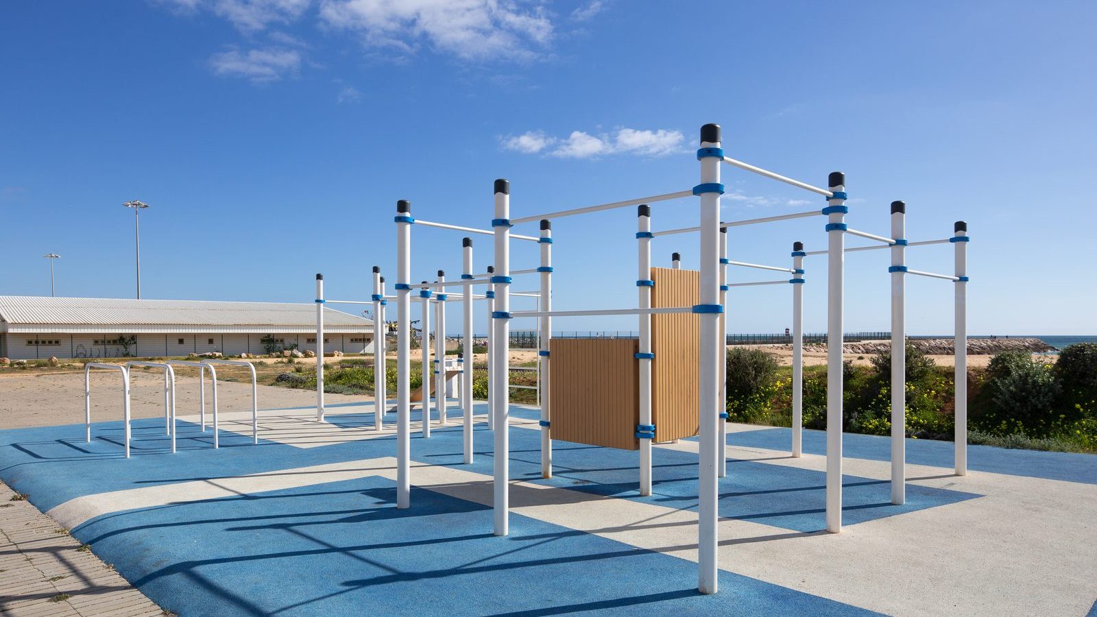 Parkour Anlage von KENGURU PRO mit hellen Pfosten, Stangen in mehreren Höhen und Wandelement auf blauem Belag an der Algarve